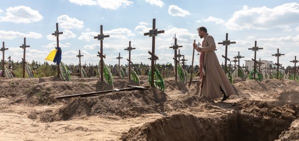 A priest overseas the burial of the remains of 13 unidentified and two identified people who were killed in the Bucha district during the Russian occupation