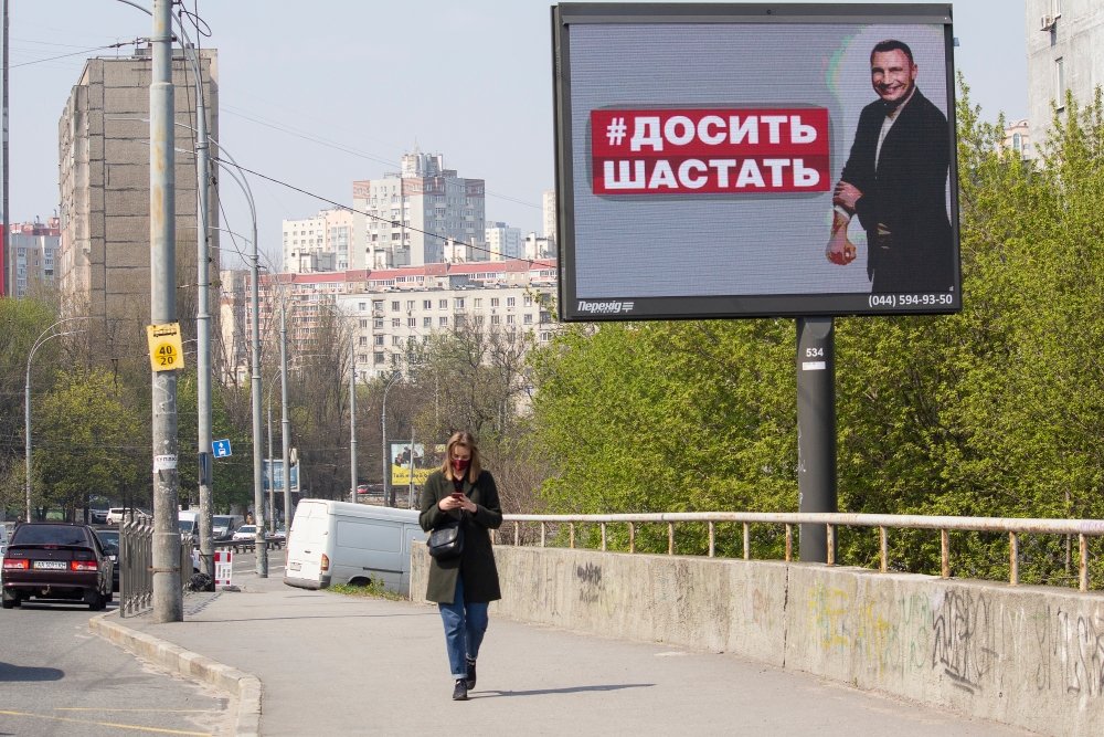 April 17 2020: Girl in a mask on a city street and a banner with the image of the mayor of Kyiv, sign reading "Do not go" in the Ukrainian language