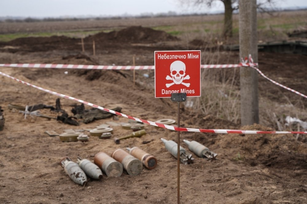 Unexploded ordinance lying in a field next to a red warning sign