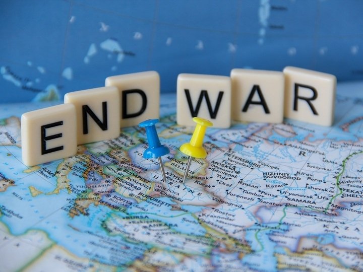 Low angle view of a sign that reads End War written with letter tiles behind yellow and blue Ukrainian flag colors push pins tacks pinned on Ukraine's map.