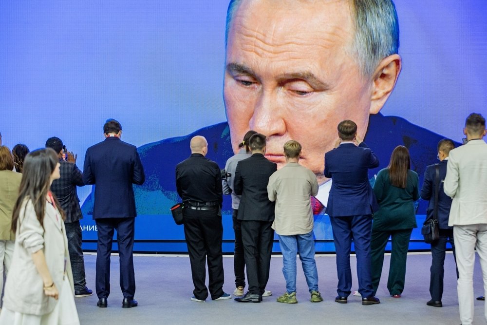 A crowd of people take pictures and watch a largescreen broadcast of President Vladimir Putin. 