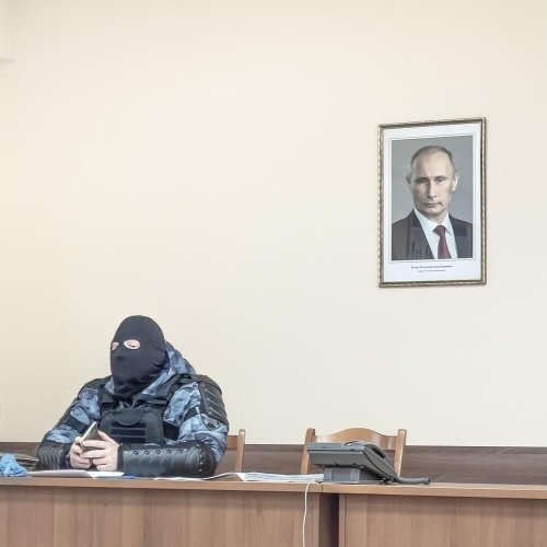 a Russian security agent sits beneath a portrait of Vladimir Putin