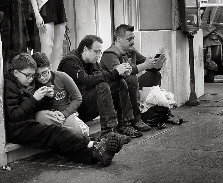 People holding smart phones while sitting. Source: Wikimedia Commons.