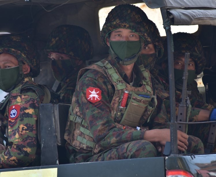 Soldiers in uniforms and masks sitting on a truck.