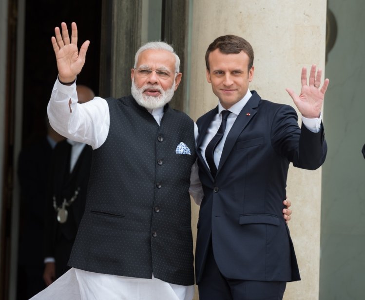 Pictured on the left is the Prime Minister of India, Narendra Modi, and on the right, the President of France, Emmanuel Macron, waving toward the camera.
