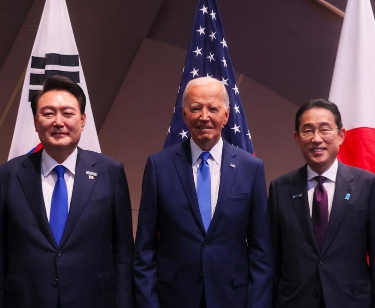 President Yoon, President Biden, and Prime Minister Kishida stand in front of their respective countries flags.