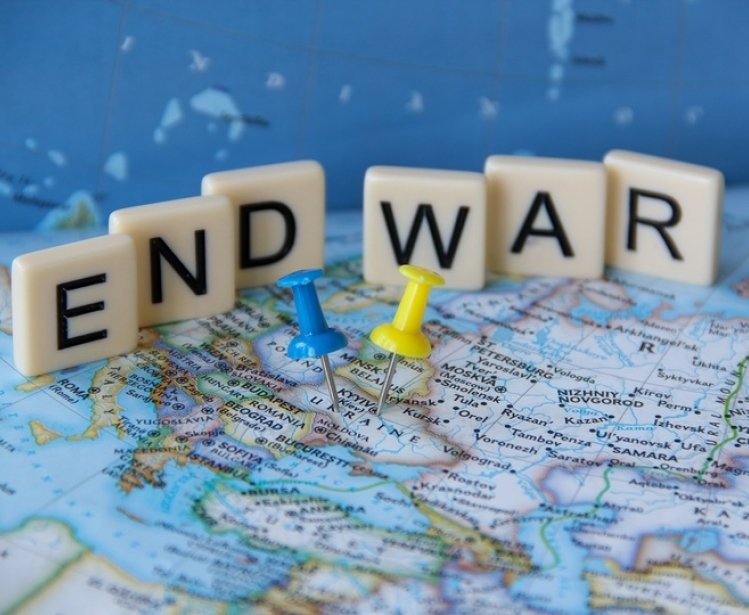 Low angle view of a sign that reads End War written with letter tiles behind yellow and blue Ukrainian flag colors push pins tacks pinned on Ukraine's map.