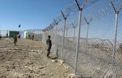 A uniformed soldier stands at a wire border fence.