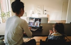 Woman working from home, with her daughter sitting by at the table, having a video conference call