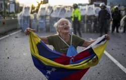 Consuelo Marquez holds a Venezuelan flag in front of police blocking demonstrations against the official election results declaring President Nicolas Maduro's reelection, the day after the vote in Caracas, Venezuela, Monday, July 29, 2024. 