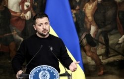 Volodymyr Zelensky speaking in front of a painting. 